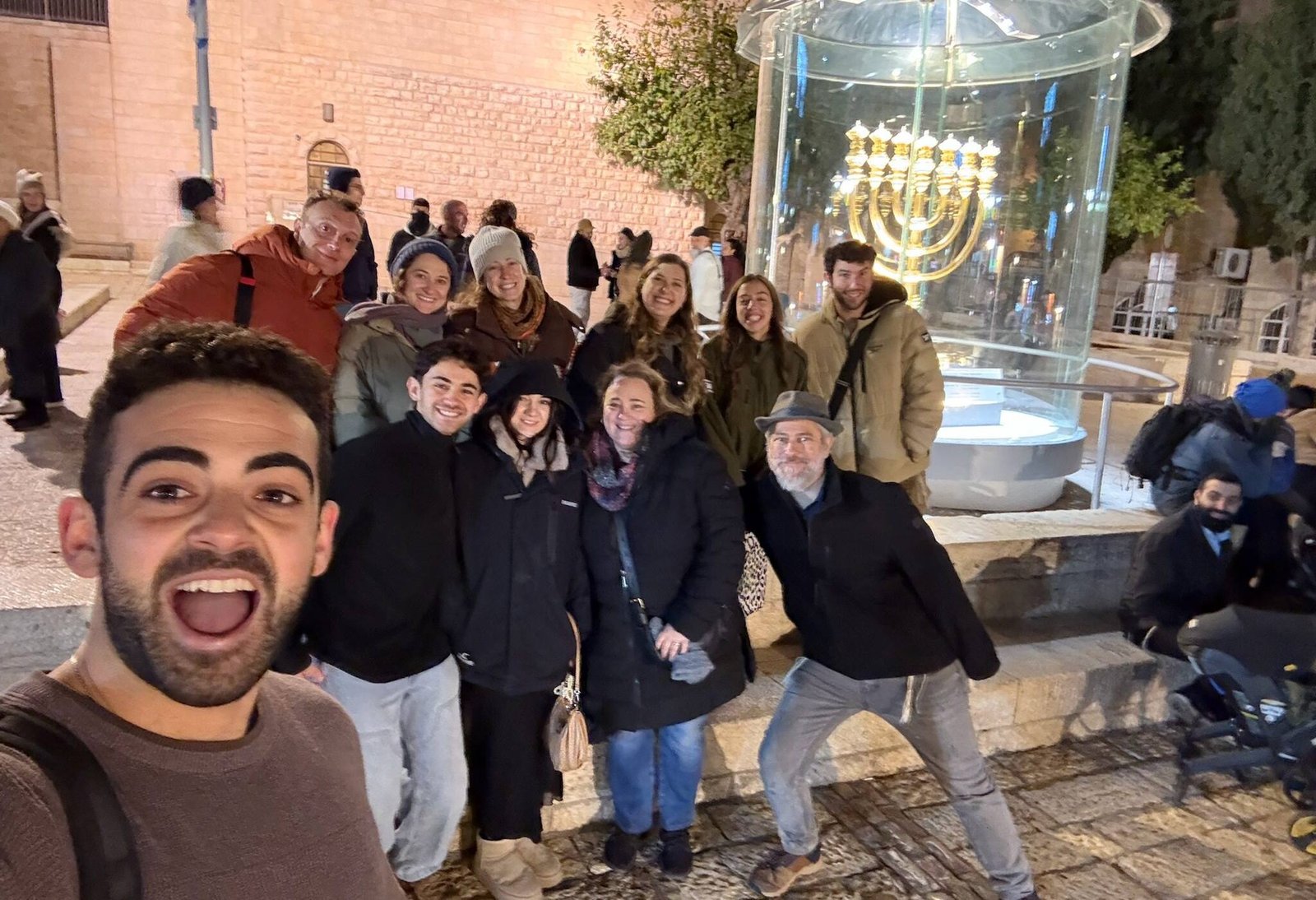 A tour group beside a lit menorah in Jerusalem at Chanukah